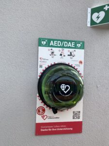 Automatisierter externer Defibrillator (AED) in einer grünen Schutzhülle an einer Wand
