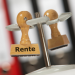 Holzstempel mit der Aufschrift „Rente“ auf einem Schreibtisch.